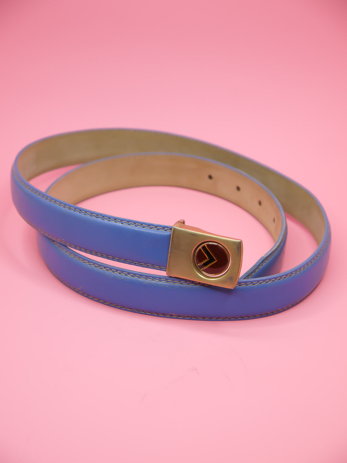 Thin blue leather belt with a push pin brass buckle featuring a chevron emblem