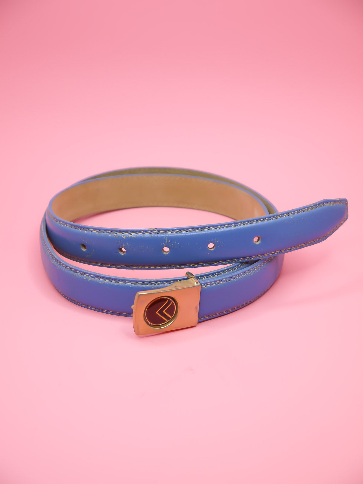 Thin blue leather belt with a push pin brass buckle featuring a chevron emblem