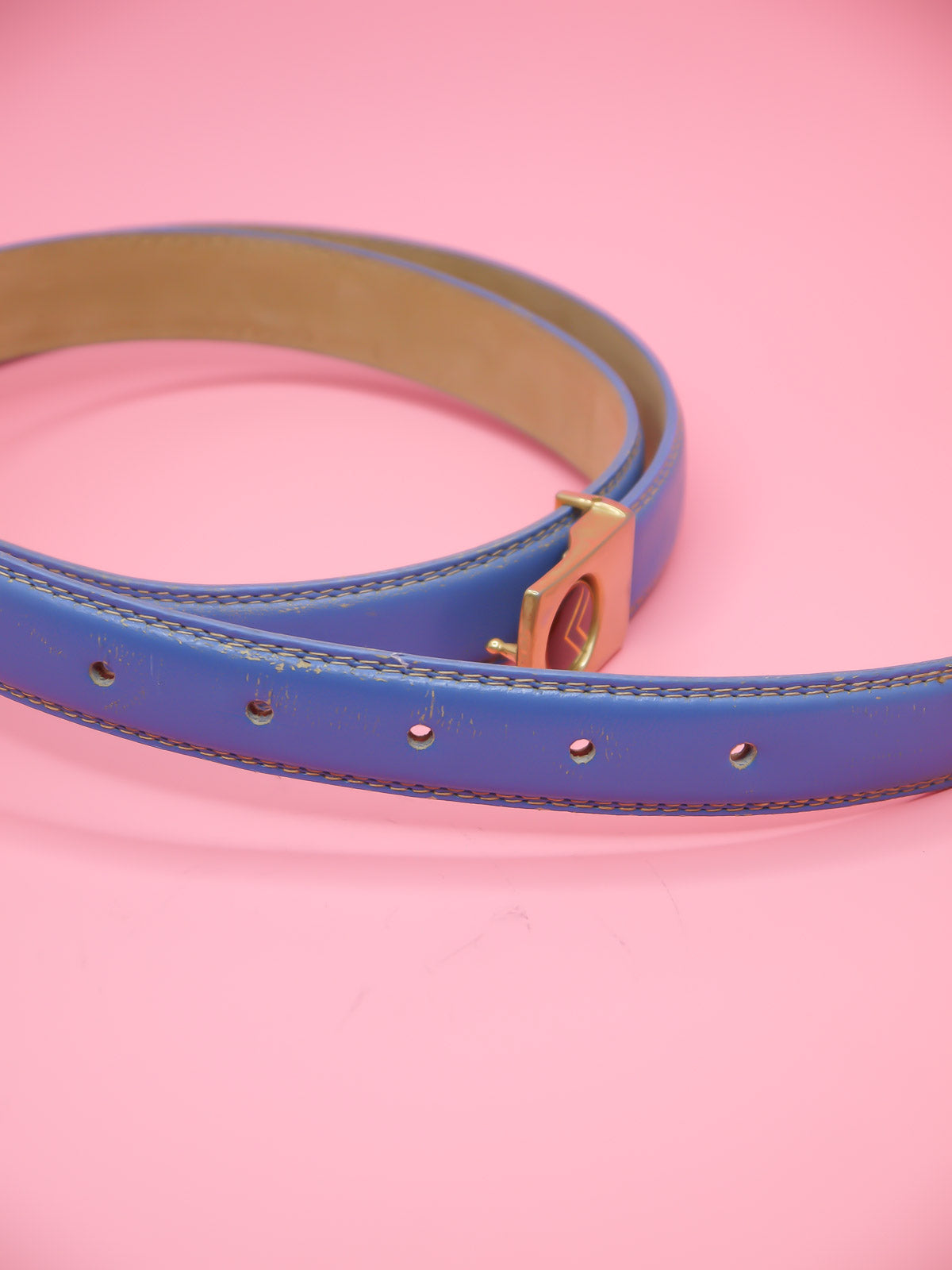 Thin blue leather belt with a push pin brass buckle featuring a chevron emblem