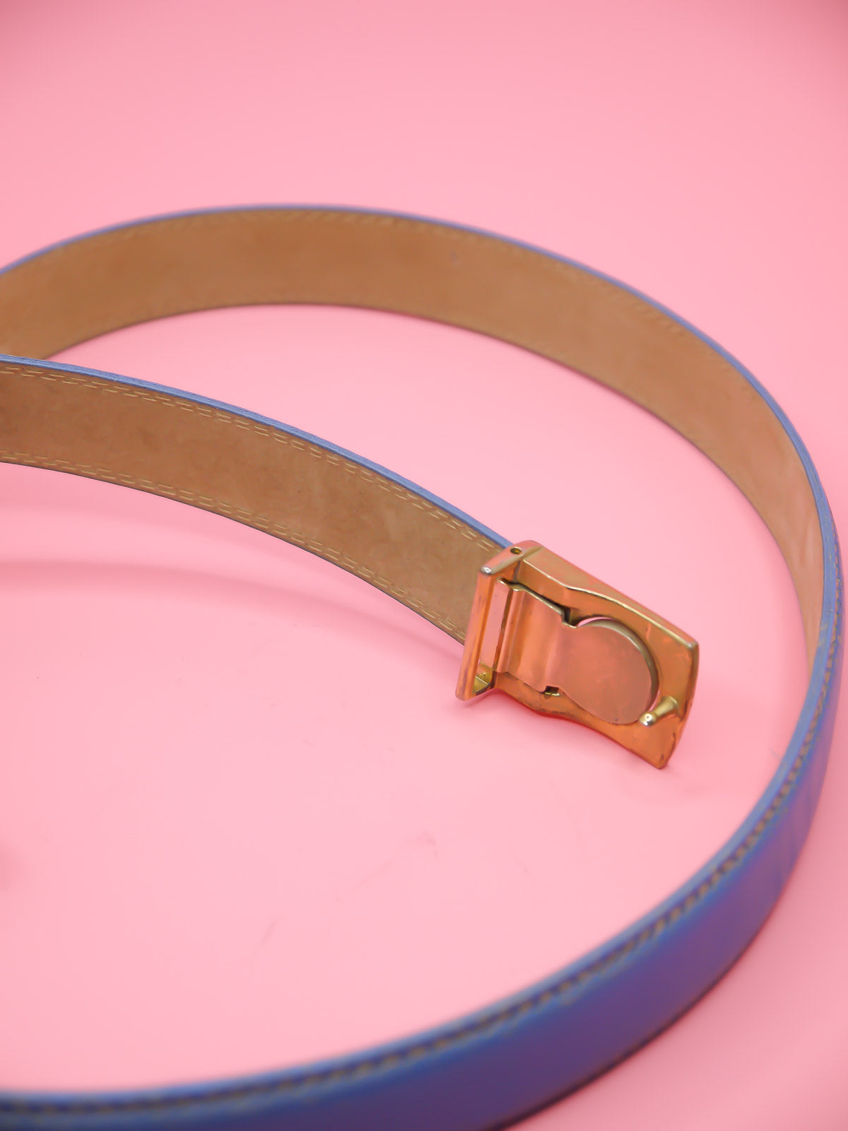 Thin blue leather belt with a push pin brass buckle featuring a chevron emblem