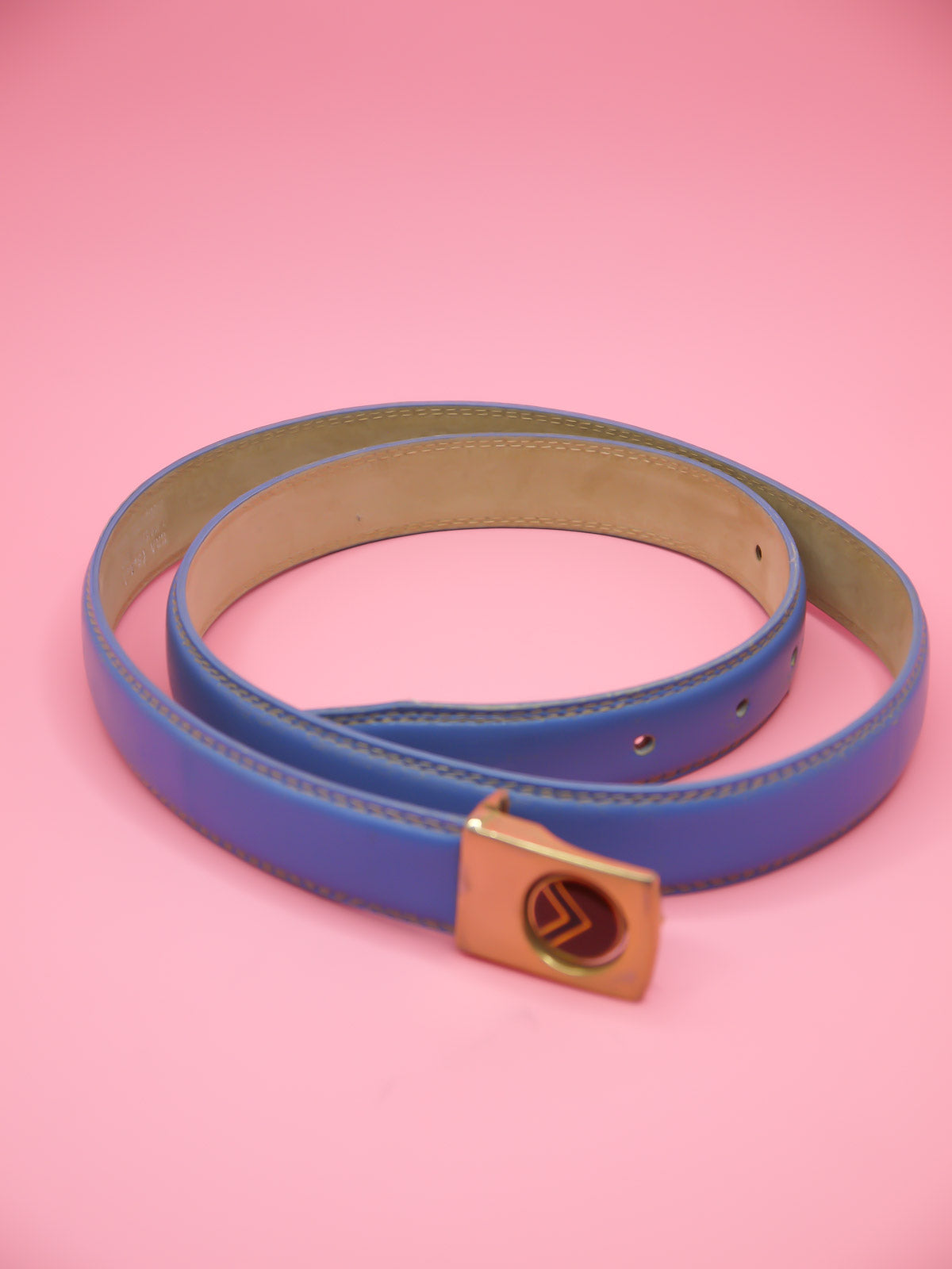 Thin blue leather belt with a push pin brass buckle featuring a chevron emblem