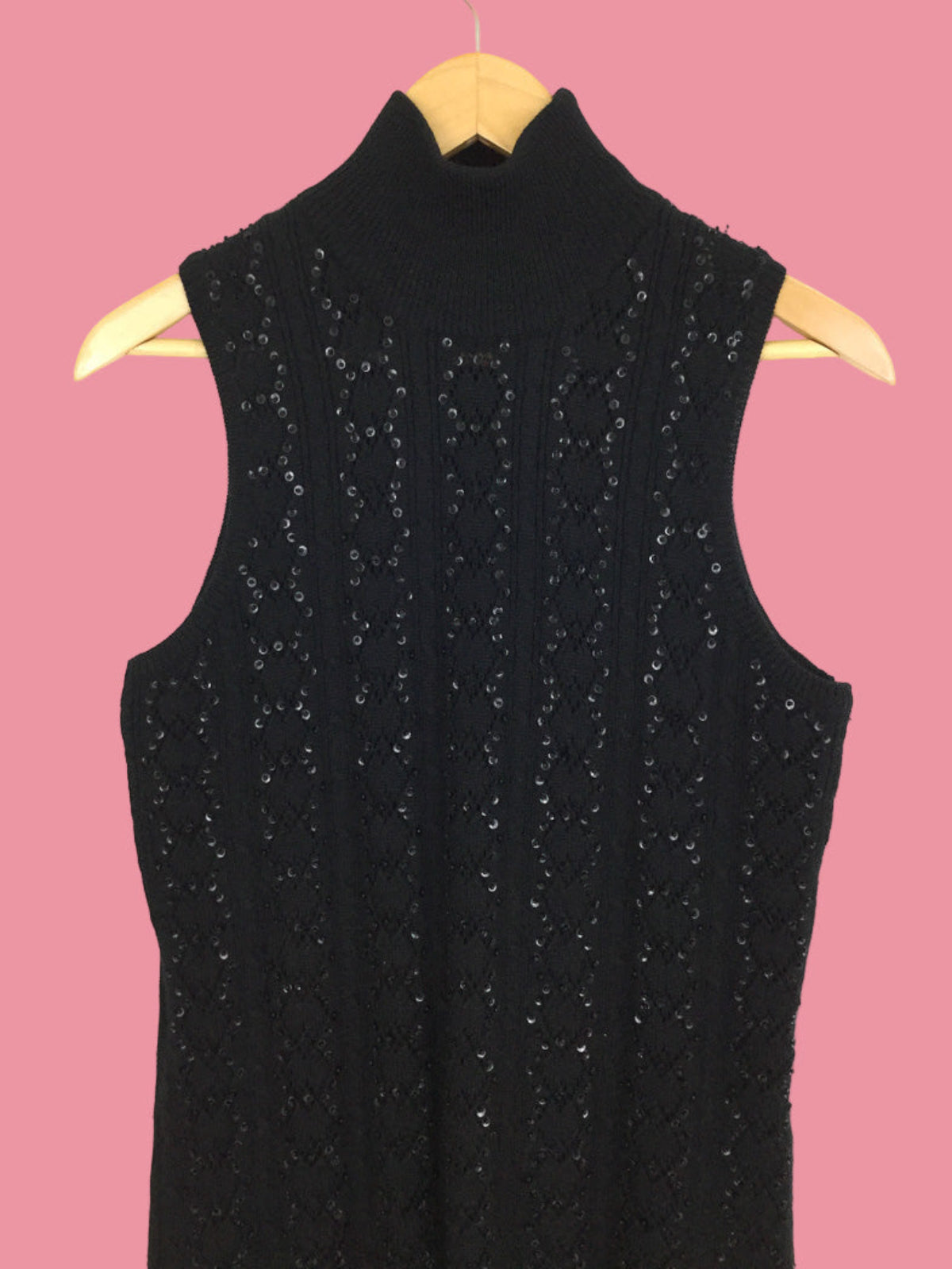 Black sleeveless dress with sequin details on a wooden hanger against a pink background
