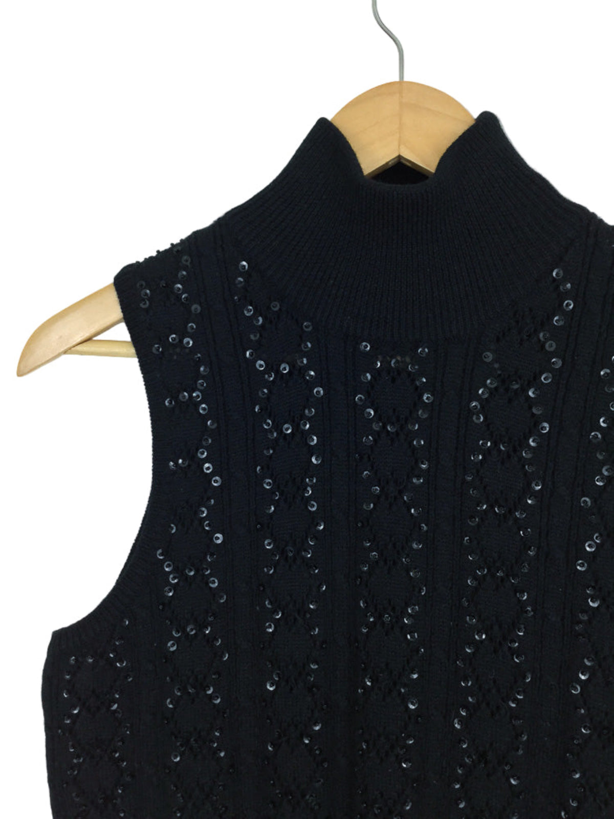 Black knitted vest with sequin embellishments on a wooden hanger against a white background