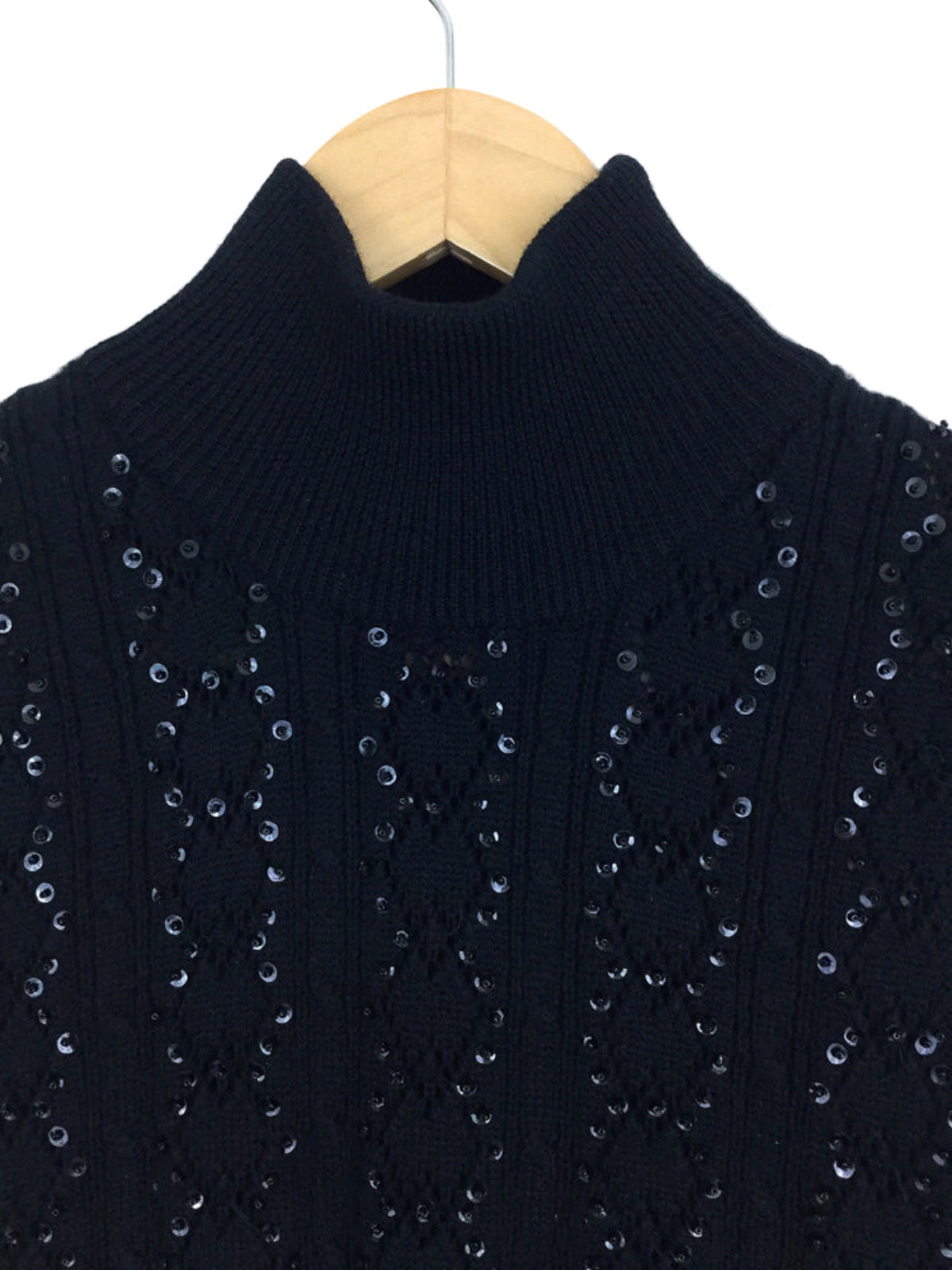 Black sweater with sequin details on a wooden hanger against a white background