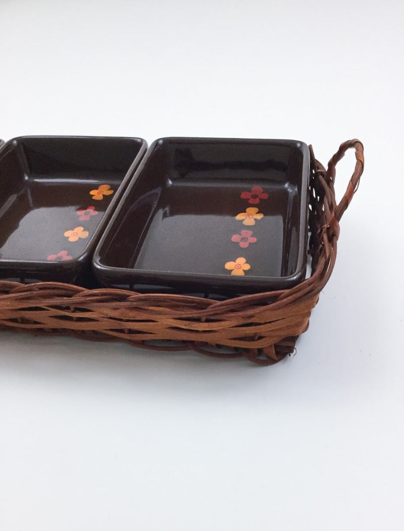 Vintage 70's brown stoneware three serving platters nestled in a brown woven basket with two handles. Serving platters have five hand painted flowers.