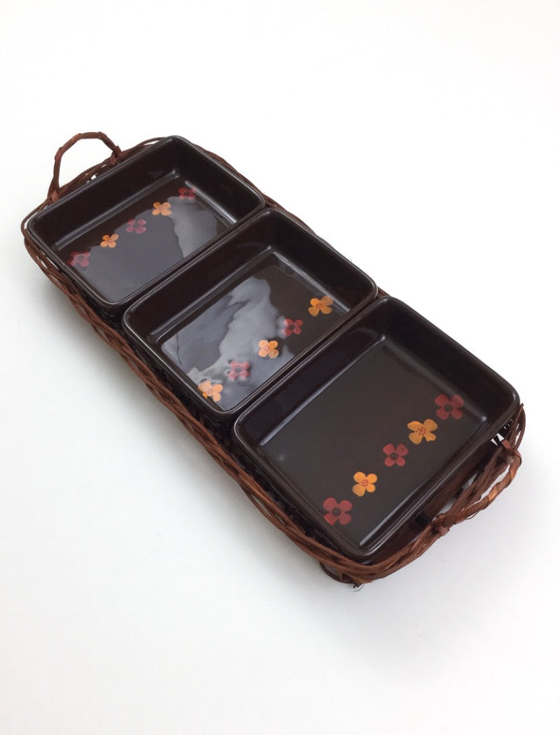 Vintage 70's brown stoneware three serving platters nestled in a brown woven basket with two handles. Serving platters have five hand painted flowers. 