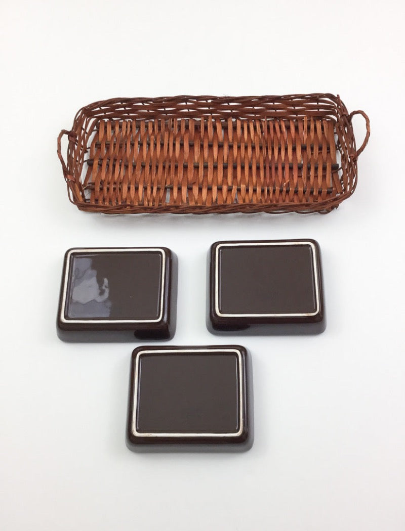 Vintage 70's brown stoneware three serving platters nestled in a brown woven basket with two handles. Serving platters have five hand painted flowers.