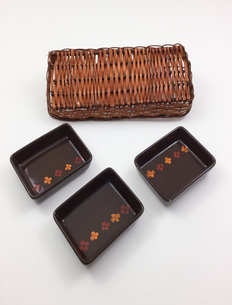 Vintage 70's brown stoneware three serving platters nestled in a brown woven basket with two handles. Serving platters have five hand painted flowers.