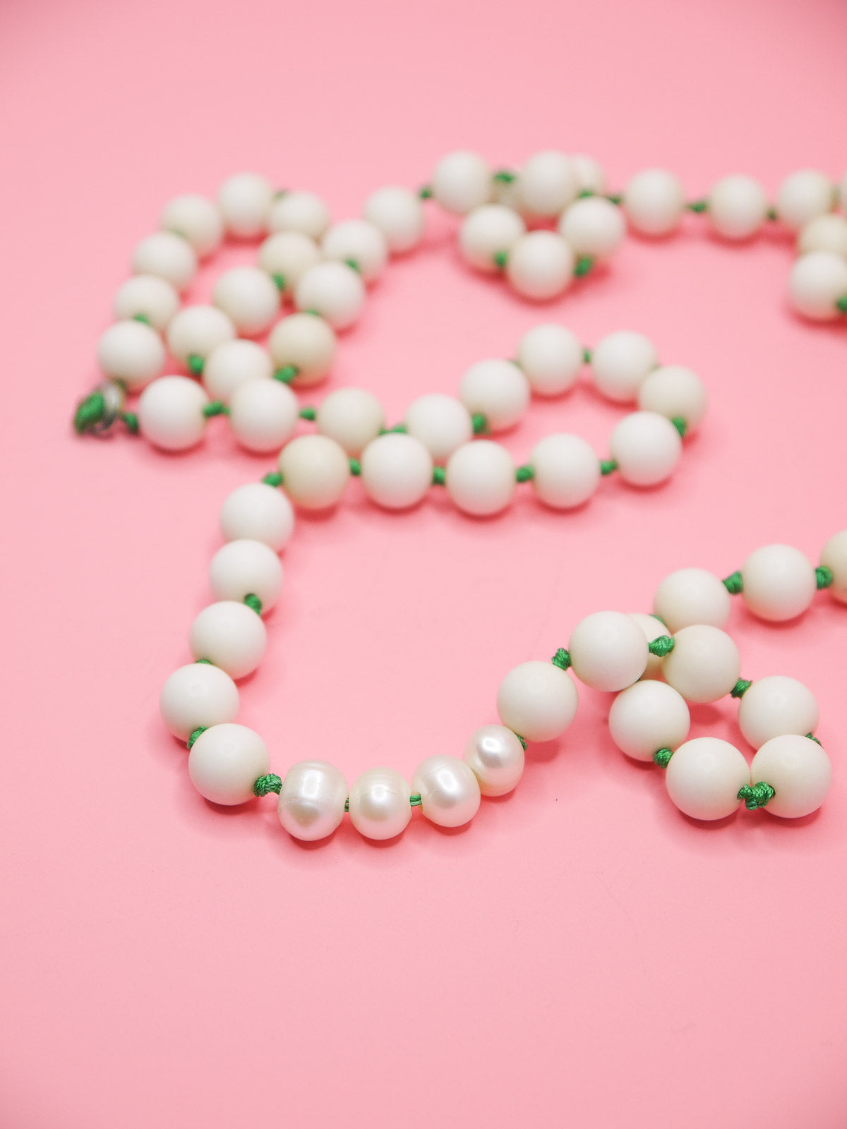 White bead necklace with green silk knots between each bead and four mother of pearl feature beads in a row.