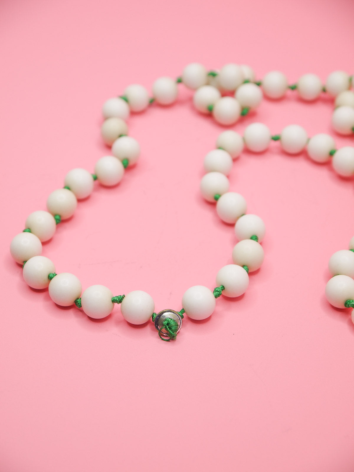 White bead necklace with green silk knots between each bead and four mother of pearl feature beads in a row.