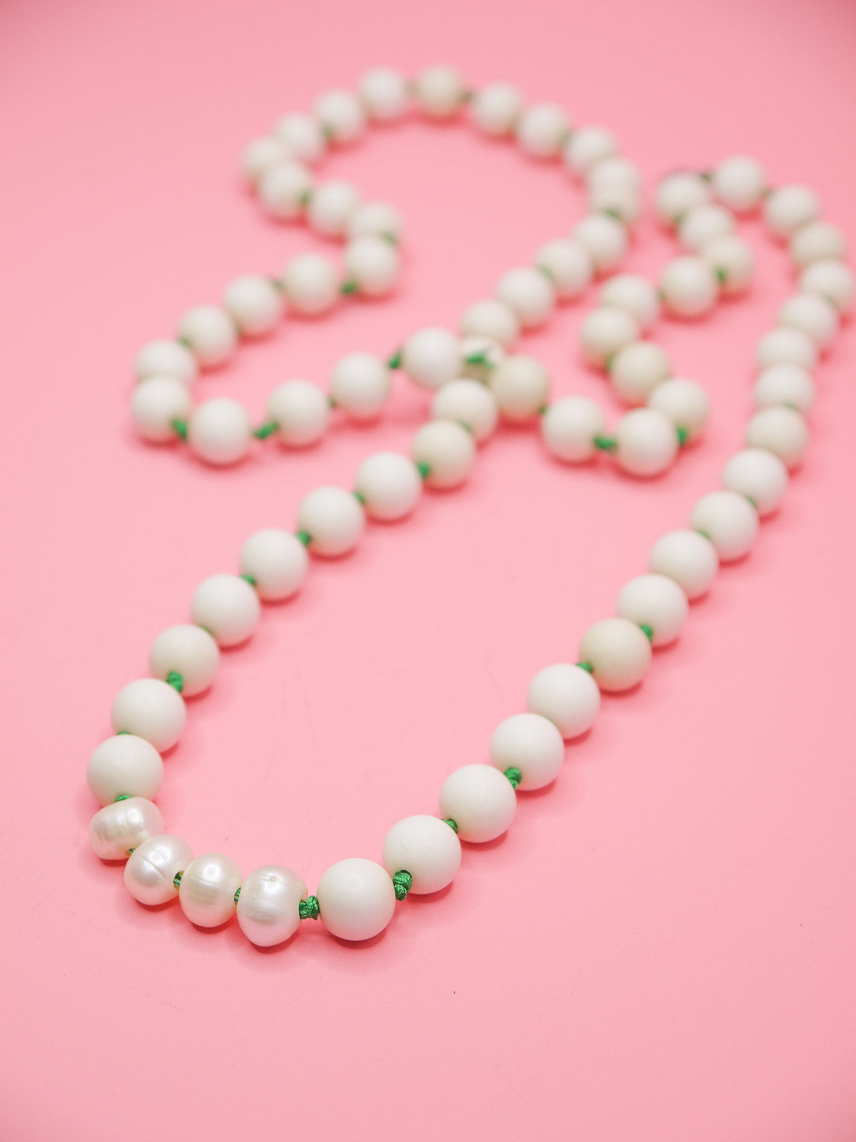 White bead necklace with green silk knots between each bead and four mother of pearl feature beads in a row.