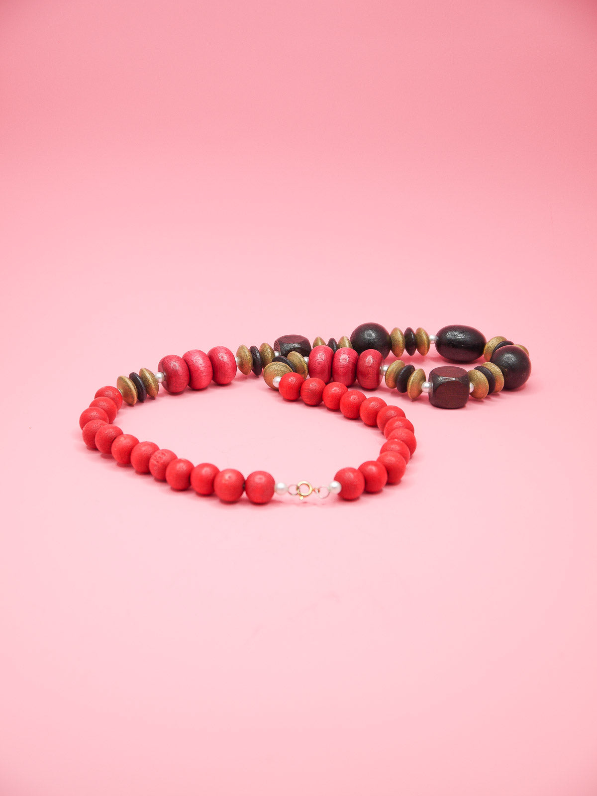 Chunky wooden bead necklace in various shapes and sizes in browns and reds with tiny pearl spacer beads and a clasp closure.