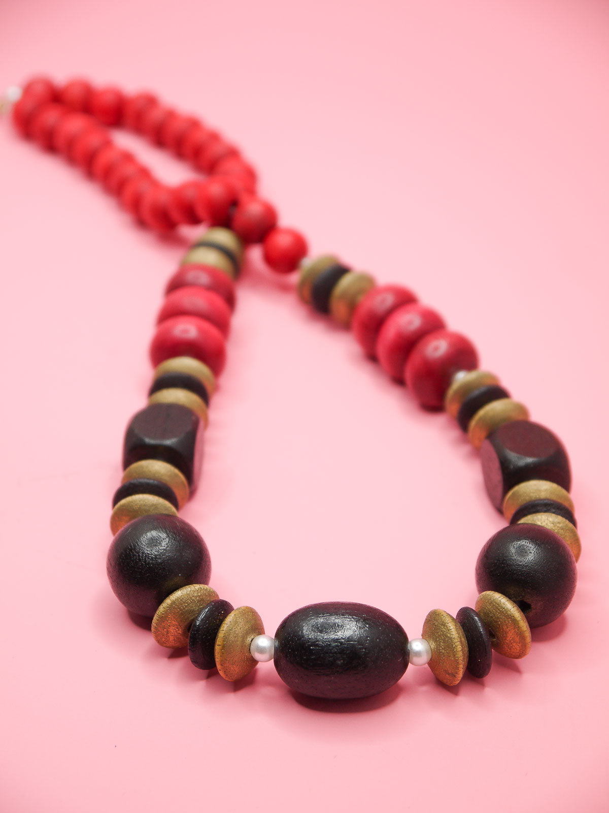 Chunky wooden bead necklace in various shapes and sizes in browns and reds with tiny pearl spacer beads and a clasp closure. 